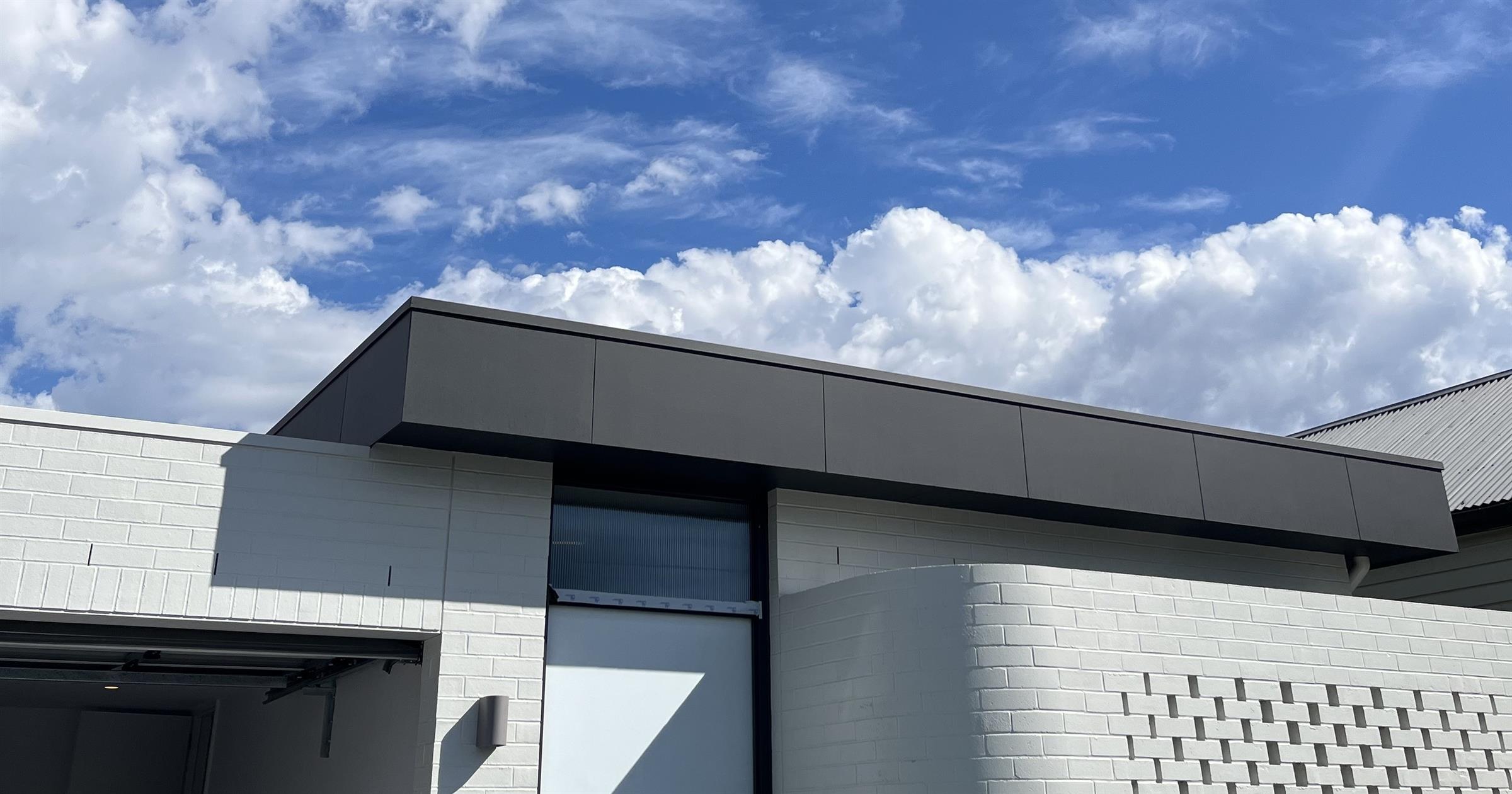 Contemporary white brick house with a dark metal fascia under a blue sky